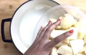Person adding chopped potatoes into a pot of water on a wooden surface.